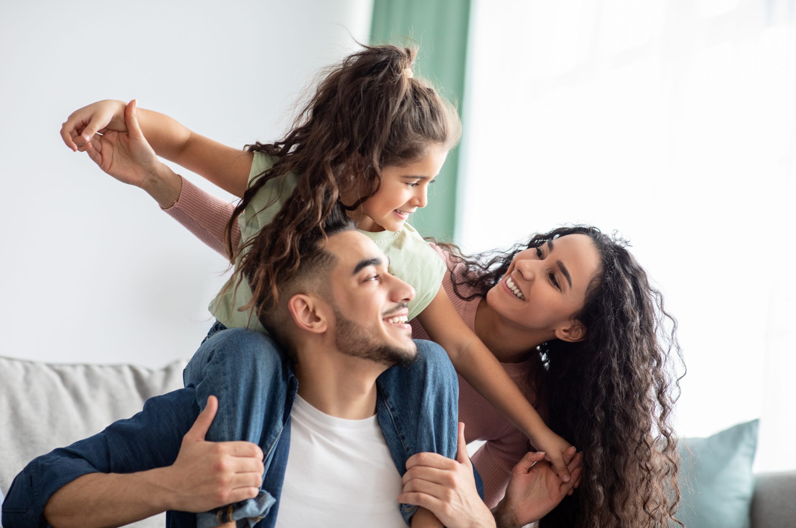 Happy mother and father play with cheerful daughter.